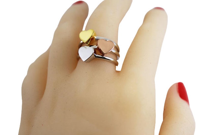 May include: A gold, silver, and rose gold ring with three heart-shaped charms.