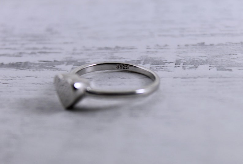May include: A silver heart-shaped ring with the inscription "S925" on the band.