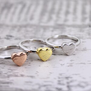 May include: Three heart-shaped rings in different colors: rose gold, gold, and silver. The rings are stacked on top of each other.