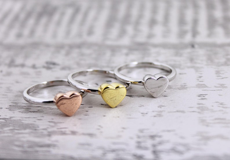 May include: Three heart-shaped rings in different colors: rose gold, gold, and silver. The rings are stacked on top of each other.