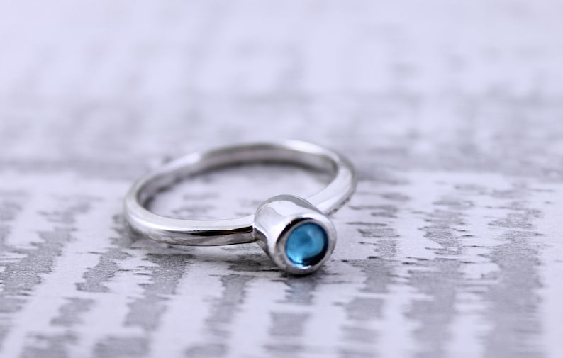 May include: A silver ring with a small, round, blue gemstone set in a silver bezel.