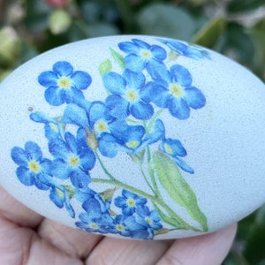 May include: A white egg decorated with blue forget-me-not flowers.