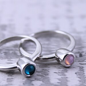 May include: Two silver rings with a blue and pink gemstone on each. The rings are stacked on top of each other.
