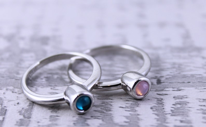 May include: Two silver rings with a blue and pink gemstone on each. The rings are stacked on top of each other.