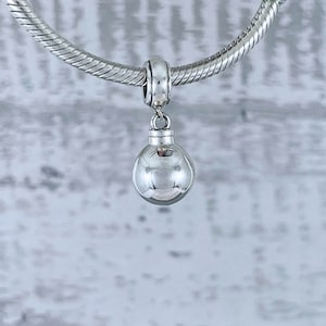 May include: A silver charm in the shape of a smooth, round ball, hanging from a silver chain.