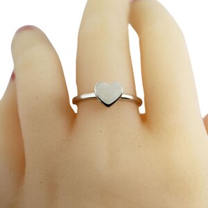 May include: A silver ring with a heart-shaped design. The ring is on a model's finger.