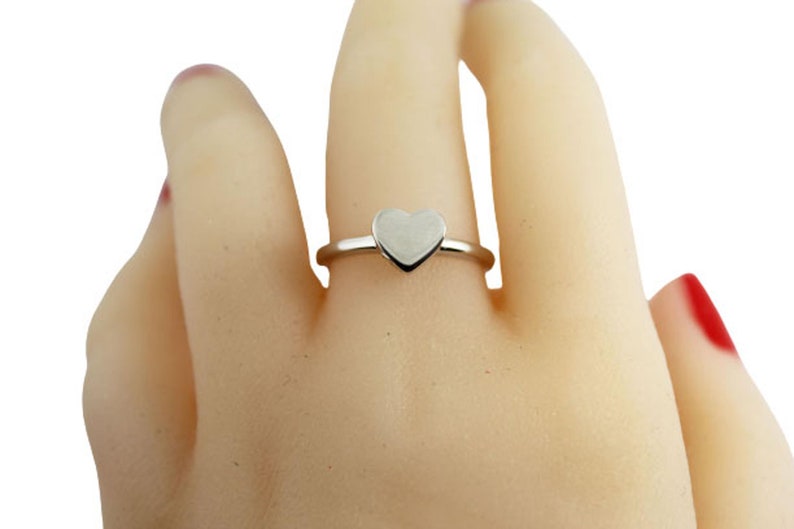 May include: A silver ring with a heart-shaped design. The ring is on a model's finger.