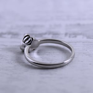 May include: A silver ring with a round, smooth stone set in the band. The ring is on a white wooden surface.