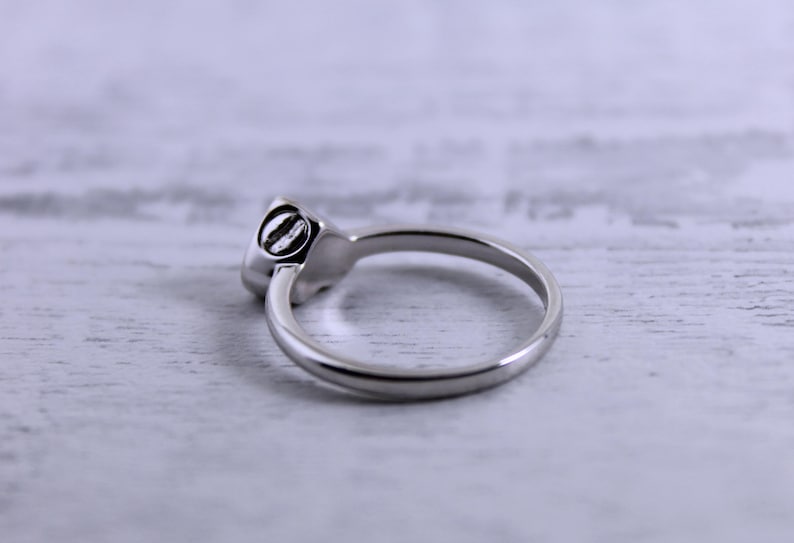 May include: A silver ring with a round, smooth stone set in the band. The ring is on a white wooden surface.