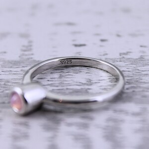 May include: A silver ring with a pink gemstone. The ring is marked with the number "S925" on the inside.