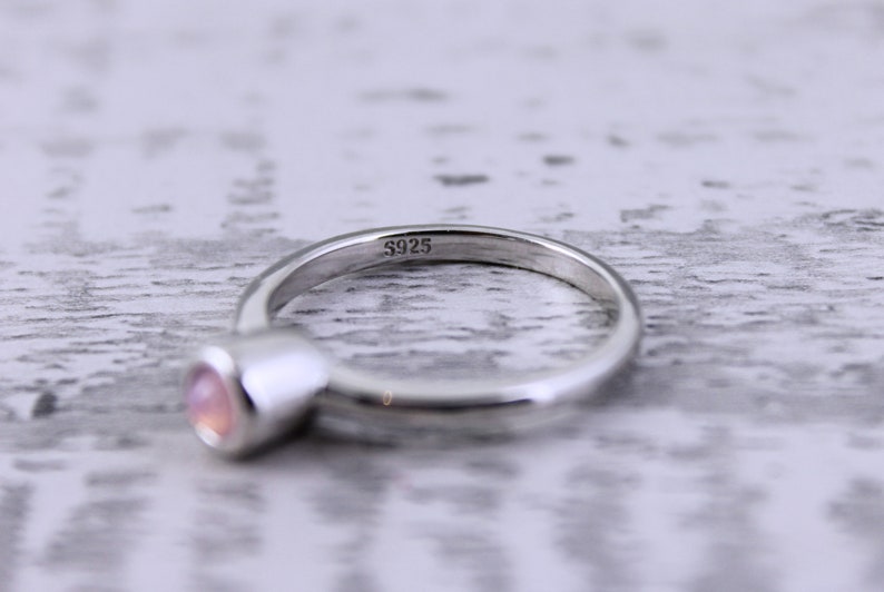 May include: A silver ring with a pink gemstone. The ring is marked with the number "S925" on the inside.