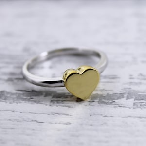 Puede incluir: Un anillo de plata con una parte superior en forma de corazón de oro.