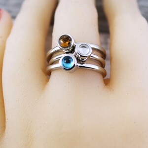 May include: A silver ring with three bands and three small gemstones. The gemstones are blue, clear, and amber.