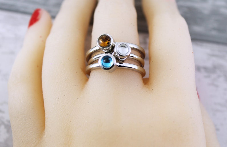 May include: A silver ring with three bands and three small gemstones. The gemstones are blue, clear, and amber.