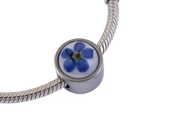 Op de afbeelding: Een zilveren armband met een ronde bedel met een blauwe vergeet-mij-nietje bloem geperst in een transparante harskoepel.