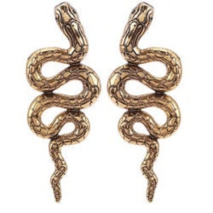 K&ouml;nnte beinhalten: Ein Paar goldfarbene Schlangenohrringe. Die Schlangen sind eingerollt und haben eine strukturierte Oberfl&auml;che.