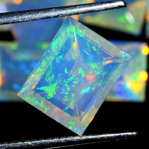 May include: A clear, rectangular, faceted opal gemstone with a green, blue, and orange iridescent sheen. The gemstone is held by tweezers.