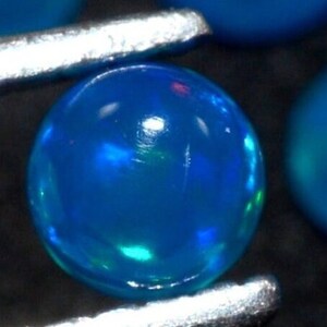 May include: A round, blue opal gemstone with a slight green iridescence. The opal is smooth and polished.