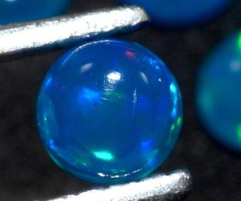 May include: A round, blue opal gemstone with a slight green iridescence. The opal is smooth and polished.