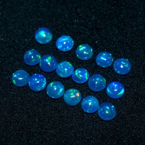 May include: A collection of 15 blue opal cabochons, each with a unique iridescent sheen. The opals are arranged in a loose pattern on a black background.