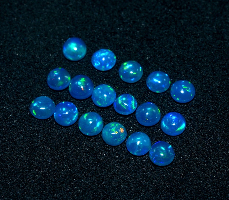 May include: A collection of 15 blue opal cabochons, each with a unique iridescent sheen. The opals are arranged in a loose pattern on a black background.