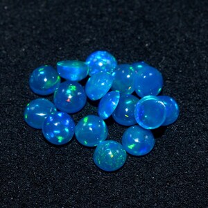 May include: A group of 15 blue opal cabochons, each with a slightly different shade of blue and iridescent flashes of color. The opals are round and smooth, and they are arranged in a loose pile.