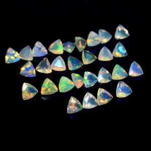 May include: A collection of iridescent, triangular-shaped opal gemstones. The opals are various shades of white, green, and blue.