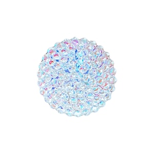 May include: A circular button featuring a dense cluster of small, clear, faceted crystals that create a shimmering, iridescent effect. The surface is highly reflective, displaying subtle rainbow-like light refractions across the rounded, textured dome shape.
