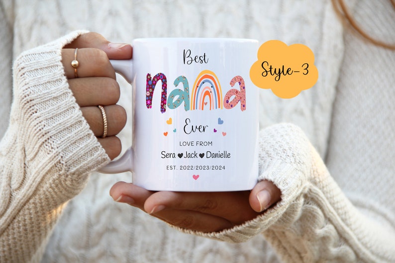 May include: White ceramic mug with the text "Best Nana Ever" in colorful letters with a rainbow and hearts. The text "Love from Sera Jack Danielle Est. 2022/2023/2024" is below the main text. The mug has a yellow cloud with the text "Style-3" in black.