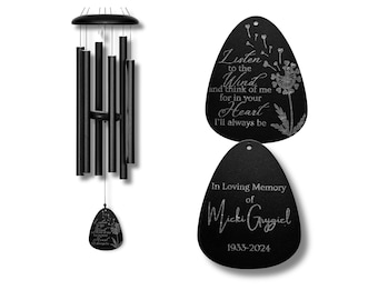 Può includere: Carillon a vento nero con un'etichetta commemorativa ovale nera. L'etichetta ha il testo "Listen to the Wind and think of me for in your Heart I'll always be" con un disegno di dente di leone. La seconda etichetta recita "In Loving Memory of Micki Grygiel 1933-2024".