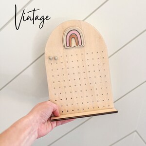 May include: Wooden earring display stand with a rainbow cutout and multiple holes for earrings. The stand is light brown and has a small base.