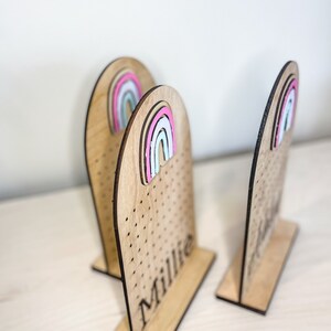 May include: Three wooden earring stands with rainbow-colored accents. The stands are personalized with the names "Millie" and "Jenna".
