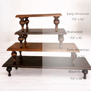 Pu&ograve; includere: Un espositore in legno a pi&ugrave; livelli in varie tonalit&agrave; di marrone e nero. Lo stand presenta quattro livelli con gambe tornite. Il testo indica le dimensioni di ogni livello, il pi&ugrave; grande misura 19 cm x 71 cm.