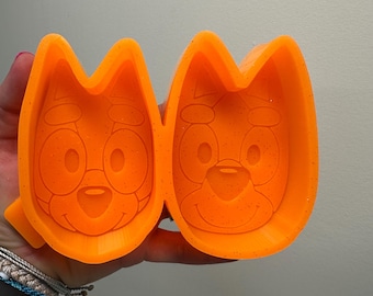 May include: Two orange silicone molds with a cartoon dog face design. The molds are detailed with a textured surface.