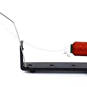 May include: A black metal thread stand with a spool of red thread and a white thread guide. The stand has a metal arm with a ring at the end.