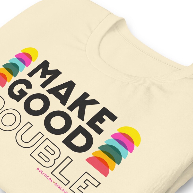 Pode incluir: Uma camiseta bege com o texto "MAKE GOOD DOUBLE" em preto. O texto &eacute; rodeado por um design colorido de semic&iacute;rculos.