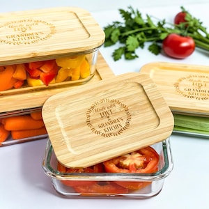 May include: Glass food storage containers with bamboo lids. The lids are engraved with the text "Made with Love in Grandma's Kitchen". The containers are filled with fresh vegetables, including carrots, bell peppers, and tomatoes.