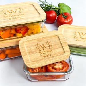 May include: Rectangular glass food containers with bamboo lids, engraved with "W" and "Williams family". The containers hold carrots, bell peppers, and tomatoes. Fresh herbs and tomatoes are visible in the background. The containers are ideal for food storage.