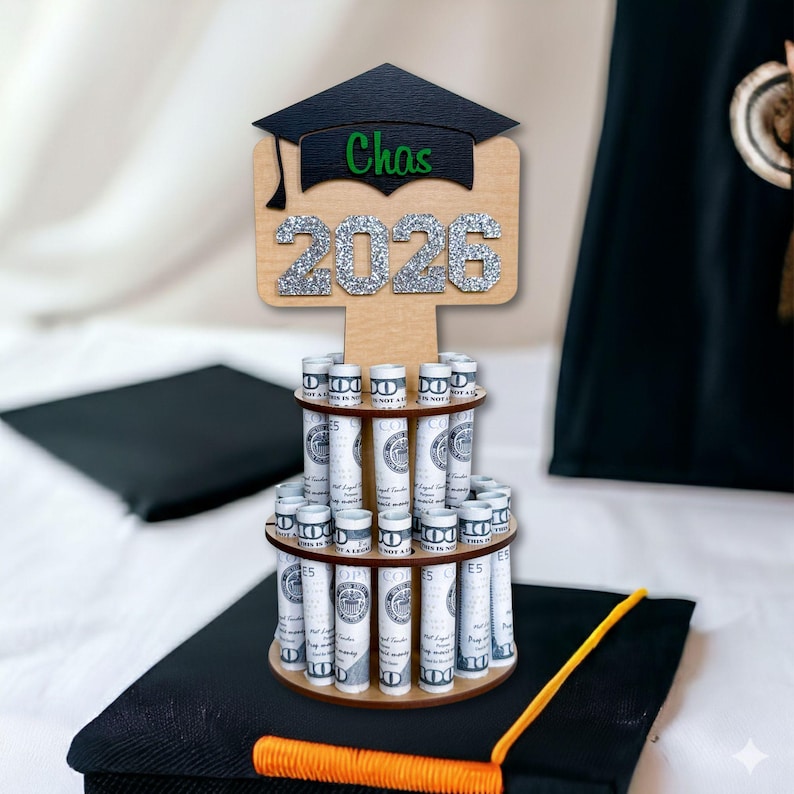 Graduation money tree gift 2026 in natural wood with silver glitter “2026” and personalized name. Wooden graduation money holder displayed on a graduation cap with rolled US dollar bills. Graduation decorations Class of 2026 cash gift for her or him.