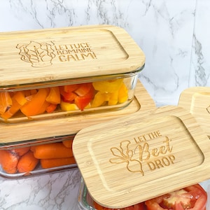 May include: Four glass containers with bamboo lids. The lids have engraved sayings: "Lettuce romaine calm!" "Let the beet drop" and a leaf design. The containers are filled with chopped vegetables.