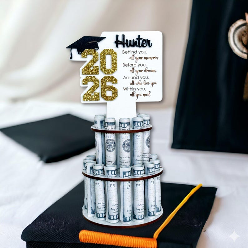 Personalized graduation money holder 2026 displayed on a graduation cap with rolled US dollar bills. Wooden graduation money tree gift with glitter “2026,” graduation cap topper, and custom name. Graduation decorations Class of 2026 cash gift for high school or college graduate.