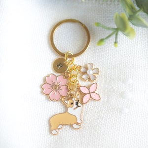 May include: Gold keychain with a pink and white flower charm, a gold charm with the letter "R", and a gold charm of a corgi.