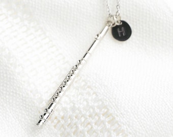 May include: A silver-toned flute pendant necklace featuring a detailed musical instrument charm and a small, circular black disc charm engraved with the letter H, suspended from a delicate silver-toned chain link necklace.