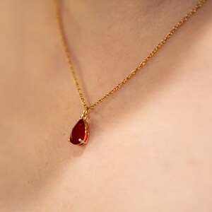 May include: A gold chain necklace with a teardrop-shaped red gemstone pendant.