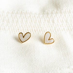 May include: A pair of gold heart-shaped earrings with white enamel. The earrings are small and delicate.