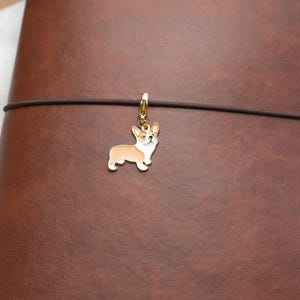 May include: A brown leather notebook with a gold-colored charm of a corgi dog attached to a black elastic band.