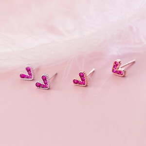 May include: Three pairs of heart-shaped earrings with pink gemstones. The earrings are made of silver and have a post back.