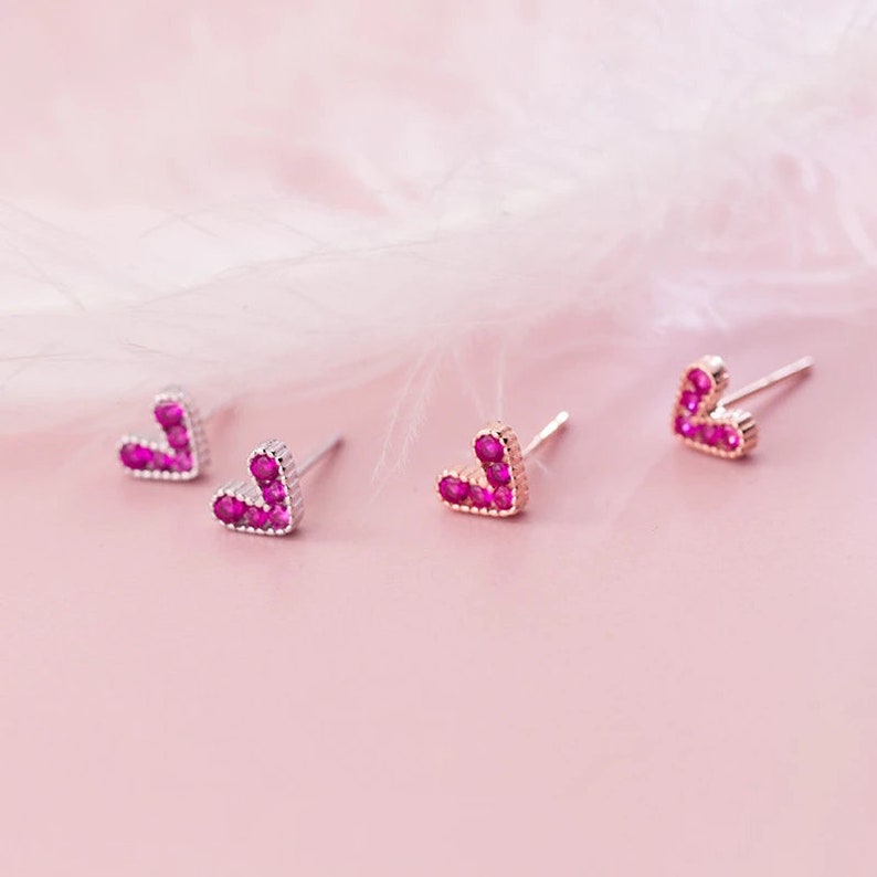 May include: Three pairs of heart-shaped earrings with pink gemstones. The earrings are made of silver and have a post back.