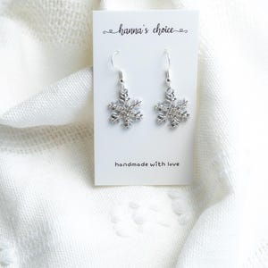 May include: Silver snowflake dangle earrings on a white card with the text "hanna's choice" and "handmade with love".