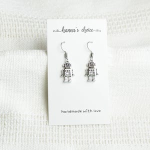May include: Silver robot earrings on a white card with the text "hanna's choice" and "handmade with love".